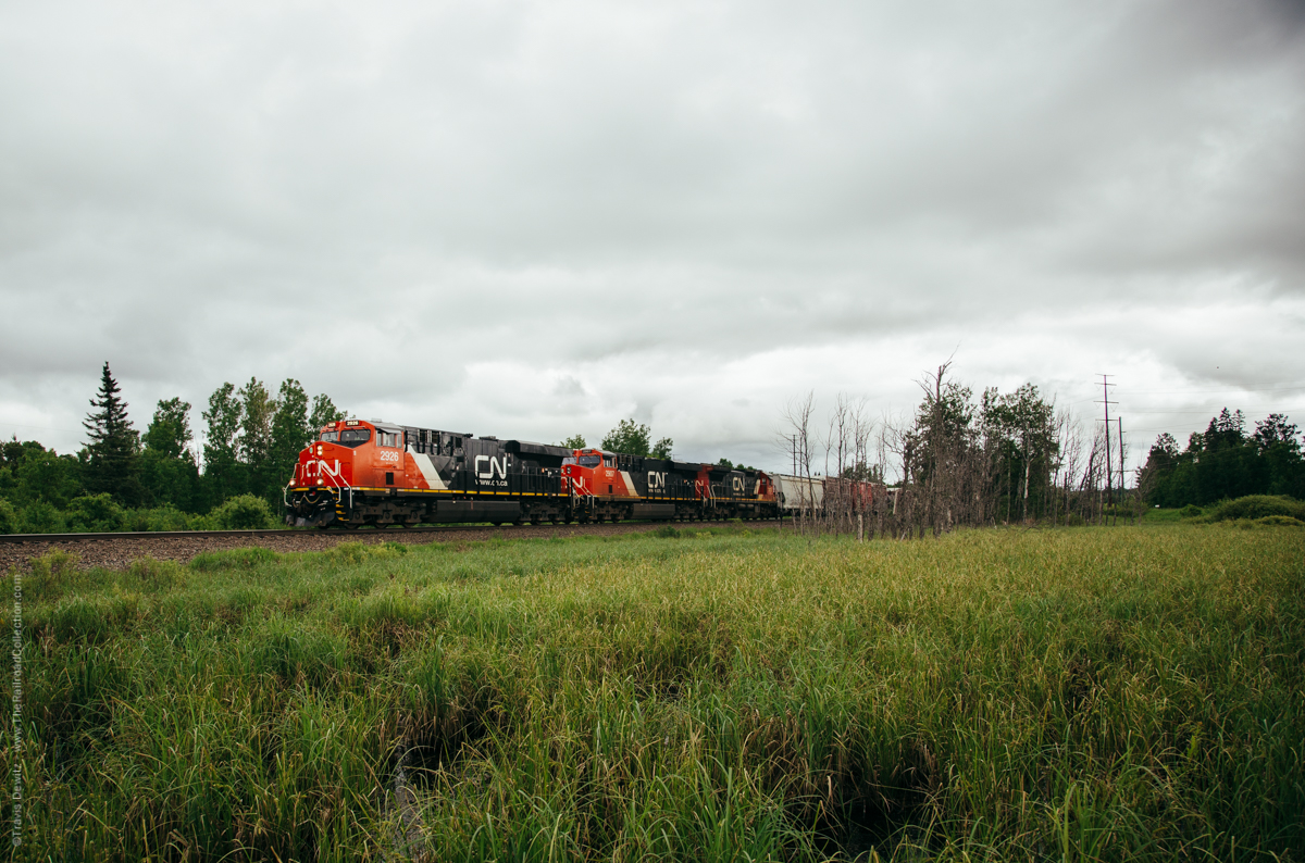 A trio of General Electric locomotives hustle this train north to Canadian National's Pokegama Yard just southwest of Superior, Wisconsin. The history of this location is slightly complicated located here in Gordon, Wisconsin. Presently this is CN's Superior Subdivision which is part of the Wisconsin Division. The Wisconsin Division is mainly everything that once was the Wisconsin Central that CN purchased in 2001. This is now CN's mainline between the Twin Ports and Chicago that handles a lot of their Canadian traffic. At this moment, the front of this train is on ex- CNW trackage and the rear is on ex-Soo trackage. The ex-Soo rightaway ran north from Ladysmith to Gordon (where it crossed over the CNW) to Ambridge (halfway between Pokegama Yard and South Itasca, just south of Superior). The ex-CNW trackage ran north from Cameron through Gordon and into South Itasca. In 1985, the Soo Line bought the Milwaukee Road and sold off portions of its system in the state which formed the Wisconsin Central. The WC gained access to the Twin Ports with trackage rights over the Soo Line from Ladysmith north. There was a non-compete clause that agreement that stated that the WC could not ship CN traffic south out of the Twin Ports. In 1992, the Wisconsin Central purchased the 98-mile Cameron to Superior line from the Chicago & North Western for $5.8 million in an effort to be able to ship the Canadian traffic south to Chicago. After this sale, the Soo Line agreed to sell its line to the WC. Now with two lines to Superior, the WC joined them at Gordon using the ex-cnw line to the north and the ex-Soo line to the south. They chose to use the ex-CNW line for the slightly better grade. The ex-Soo right-a-way is now the Wild Rivers Trail and is just out of the frame to the right. The cement bridge abutments are still left standing just beyond the trees in the center of the frame where the Soo once crossed over the CNW. The third unit in this consist is an ex-CNW C40-8 which may have o