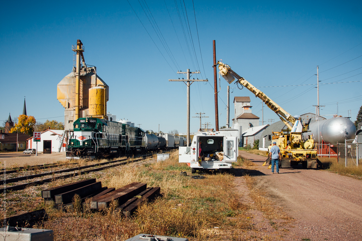 Wisconsin Northern departs Bloomer, Wisconsin towards Norma as a utility company worker stops to watch before contining to set a utility pole.